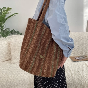 Detail of a large brown sherpa tote bag with green stripes and metal logo plate