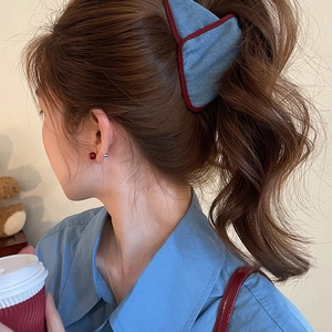 Detailed view of a blue denim bow hair claw with red trim on model's braided hair