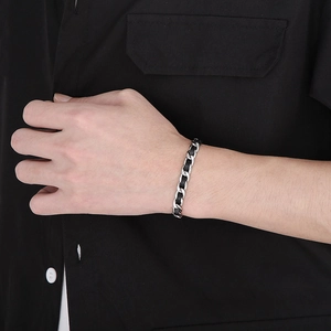 Détail du bracelet gourmette NK avec cuir noir tressé porté sur un poignet masculin