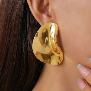 Close-up of oversized gold irregular wavy metal earrings on a model's ear