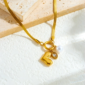 Elegant gold snake chain necklace with heart, pearl and gemstone pendants on stone base