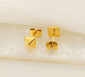 Vue macro de boucles d'oreilles pyramides carrées dorées sur surface en marbre blanc