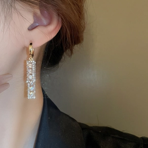 Detail showing long rectangular gold zircon earrings worn on a model's ear