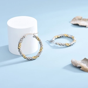 Orecchini a cerchio bicolore oro e argento ritorti su uno sfondo blu minimalista