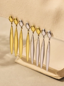 Macro shot of polished gold and silver long teardrop earrings on a beige stand