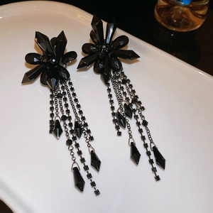 Macro shot of elegant black crystal flower earrings with long tassels on white porcelain