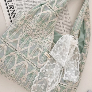 Detail of light green canvas tote bag featuring intricate floral lace and white bow