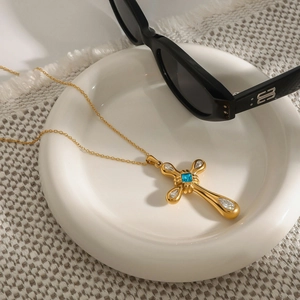 18k gold stainless steel cross necklace with blue gemstone on white ceramic tray