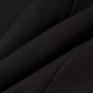 Dettaglio del tessuto strutturato nero che mostra la trama fine e il drappeggio del completo