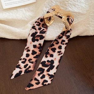Macro detail of golden textured metal hair clip with elegant leopard print ribbon fabric