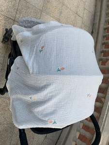 Detail of white cotton muslin stroller cover with orange and green floral embroidery