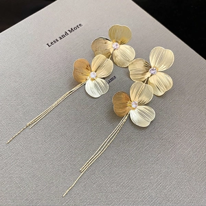 Close-up of golden hollow flower earrings with tassel chains and brushed metal finish