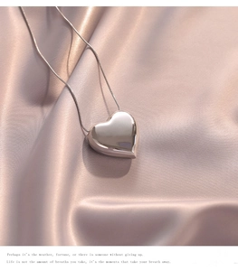 Macro detail of high-polish heart pendant with fine snake chain on champagne silk fabric