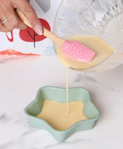 Detailed view of pink polka dot silicone spatula pouring batter into star-shaped molds