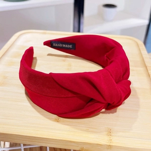 Wide solid red knotted fabric headband with a handmade label on a wooden tray