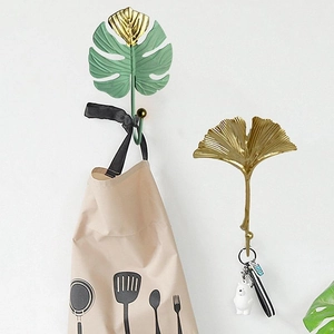 Mini wall hooks in green monstera and gold ginkgo leaf shapes on a white wall