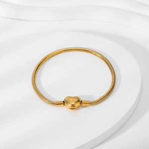 Detail of 18K gold snake chain bracelet featuring a heart-shaped clasp on white stand