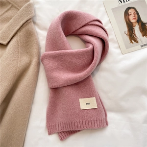 Detail showing pink knitted scarf with 'emo' fabric label on white textured background