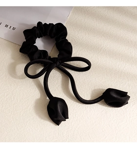 Detail of black satin scrunchie with large bow and tulip charms on a textured background