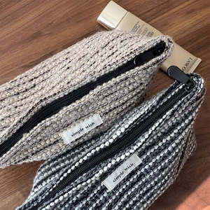Close-up of thick tweed makeup bags in beige and black-white blends on wood surface