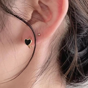 Close-up of a heart-shaped earring with black enamel and gold finish worn by a model