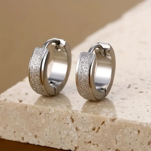 Macro shot of silver stainless steel matte hoop earrings on stone textured background