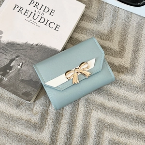 Detail of light blue tri-fold wallet with gold bow hardware and white V-stitch leather trim