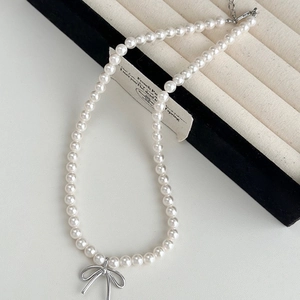 Close-up of elegant white pearl necklace featuring a silver bow pendant on a display