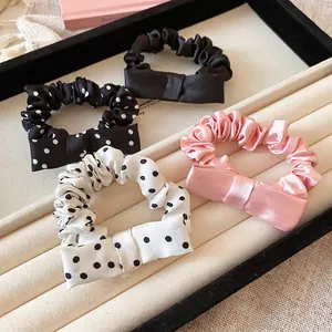 Set of 4 elegant satin polka dot bow scrunchies in black, white and pink displayed on a tray