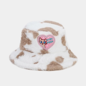 Close-up of fluffy cow print bucket hat featuring a pink heart and cat embroidery patch