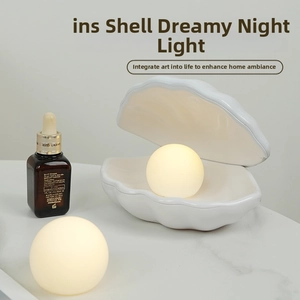 Detail of a white ceramic shell night light with a warm glowing sphere on a bedside table
