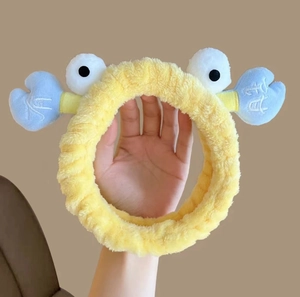 Detail of yellow plush headband with blue crab claw decor and decorative text