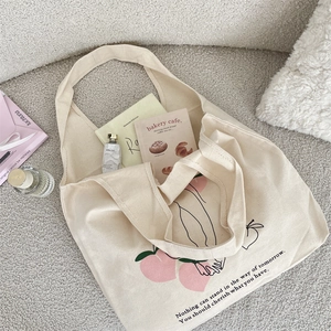 Close-up of cream canvas tote bag featuring peach print and quote on a textured surface