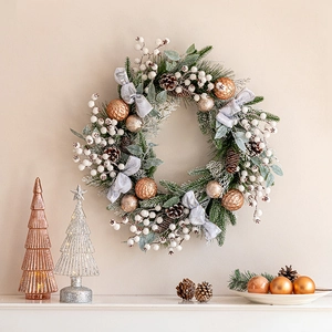 Christmas wreath with bronze baubles, pine cones, and silk ribbon on a warm wall