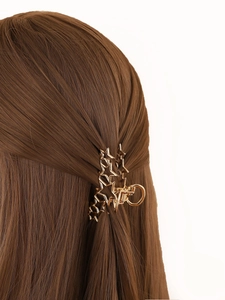 Detail of a golden star-shaped shark clip worn on long brown hair with metallic finish