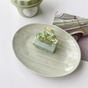 Detail view of a square marble green acetate hair claw clip on a ceramic tray