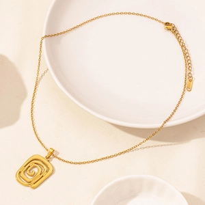 Macro shot of gold stainless steel geometric spiral pendant on a minimalist ceramic plate