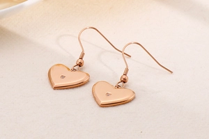 Macro shot of rose gold heart earrings with a central crystal on fabric background