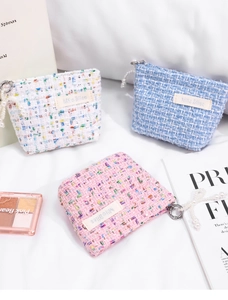 Detailed view of tweed cosmetic pouches in pink, blue, and white with pearl zippers
