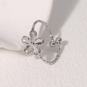 Detail of silver floral open ring with textured band and flower motif on white stage