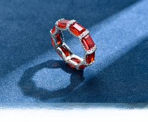 Macro shot of rectangular red gemstone silver eternity ring on textured navy fabric