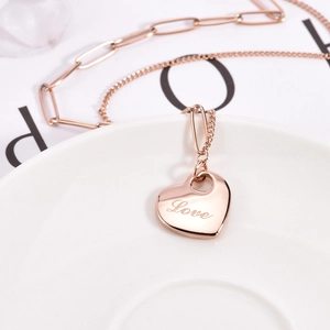 Rose gold layered heart necklace with Love engraving on a white ceramic plate
