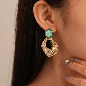 Close-up of vintage gold floral earrings with green gemstone and pearls on model
