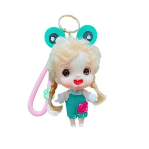 Cute cartoon doll keychain with golden pigtails and green frog hat on white background