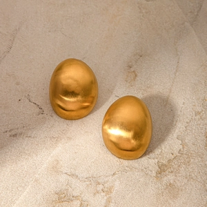 Macro shot of oval brushed 18k gold earrings resting on a natural beige stone texture