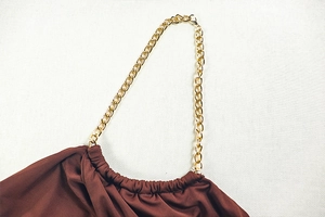 Detail of a brown bodycon dress featuring a gold metal chain strap on white fabric