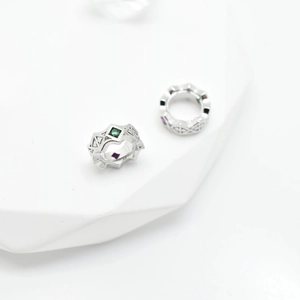 Silver geometric ring charms with green and purple square gemstones on white pedestal
