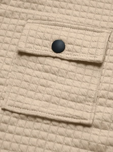 Detail of beige quilted fabric featuring diamond texture and a matte black button pocket