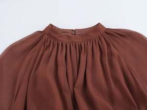 Dettaglio del collo alto a pieghe e della chiusura con bottone su un abito in chiffon marrone