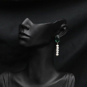 Close-up of elegant drop earrings featuring a green faceted gem and five white pearls